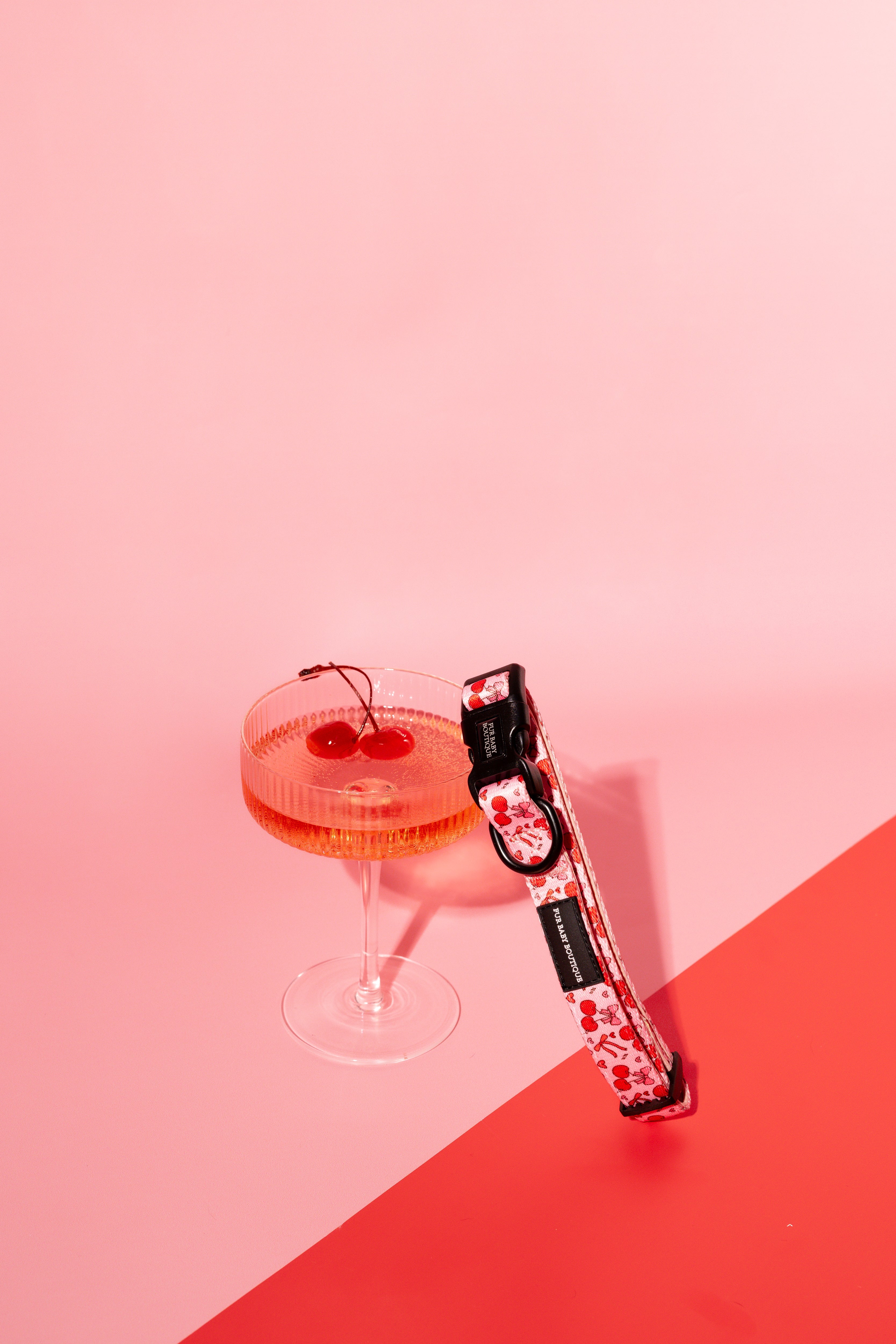 Cocktail with cherries and a pink dog collar and red background